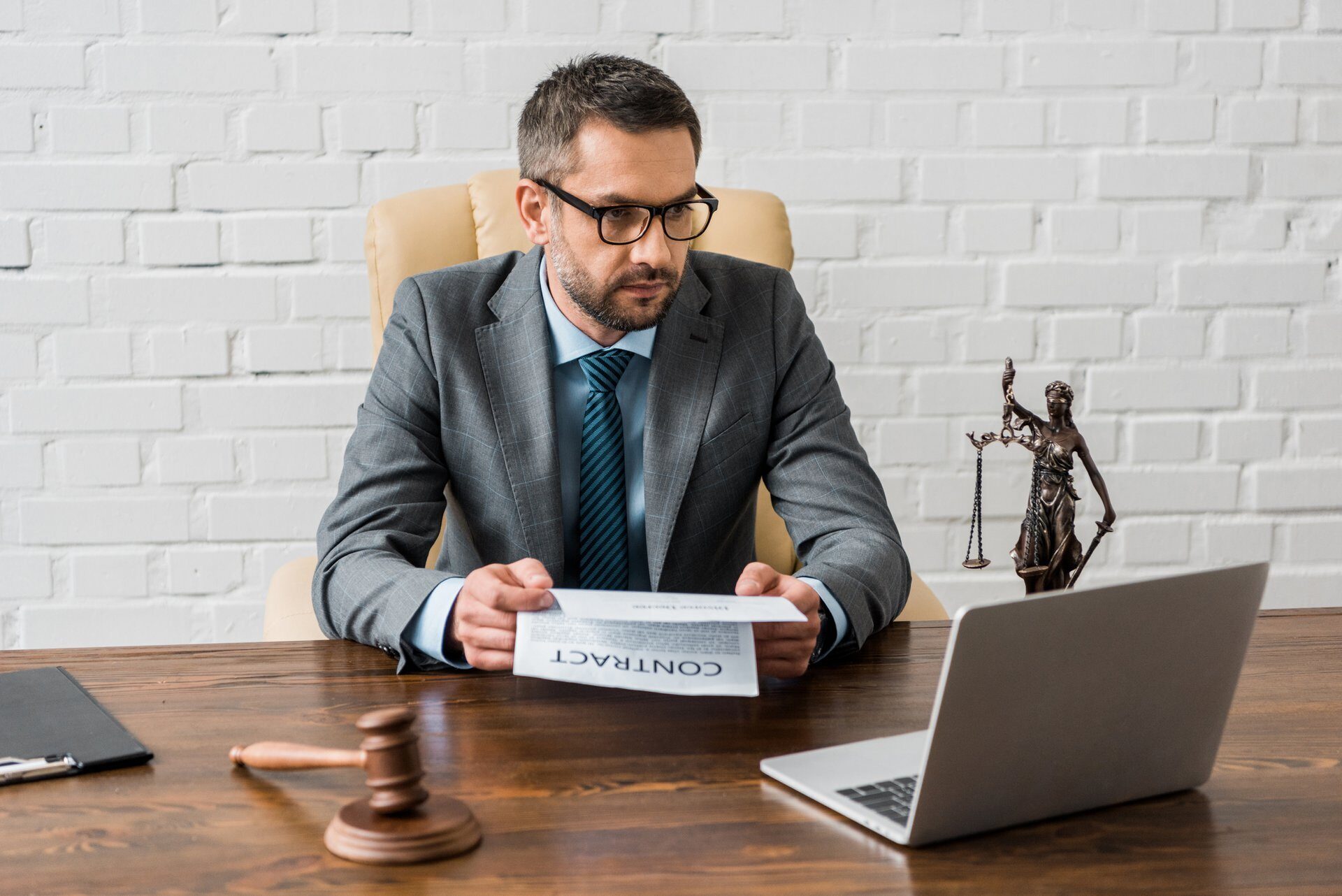 serious male lawyer holding contract and looking at laptop in office
